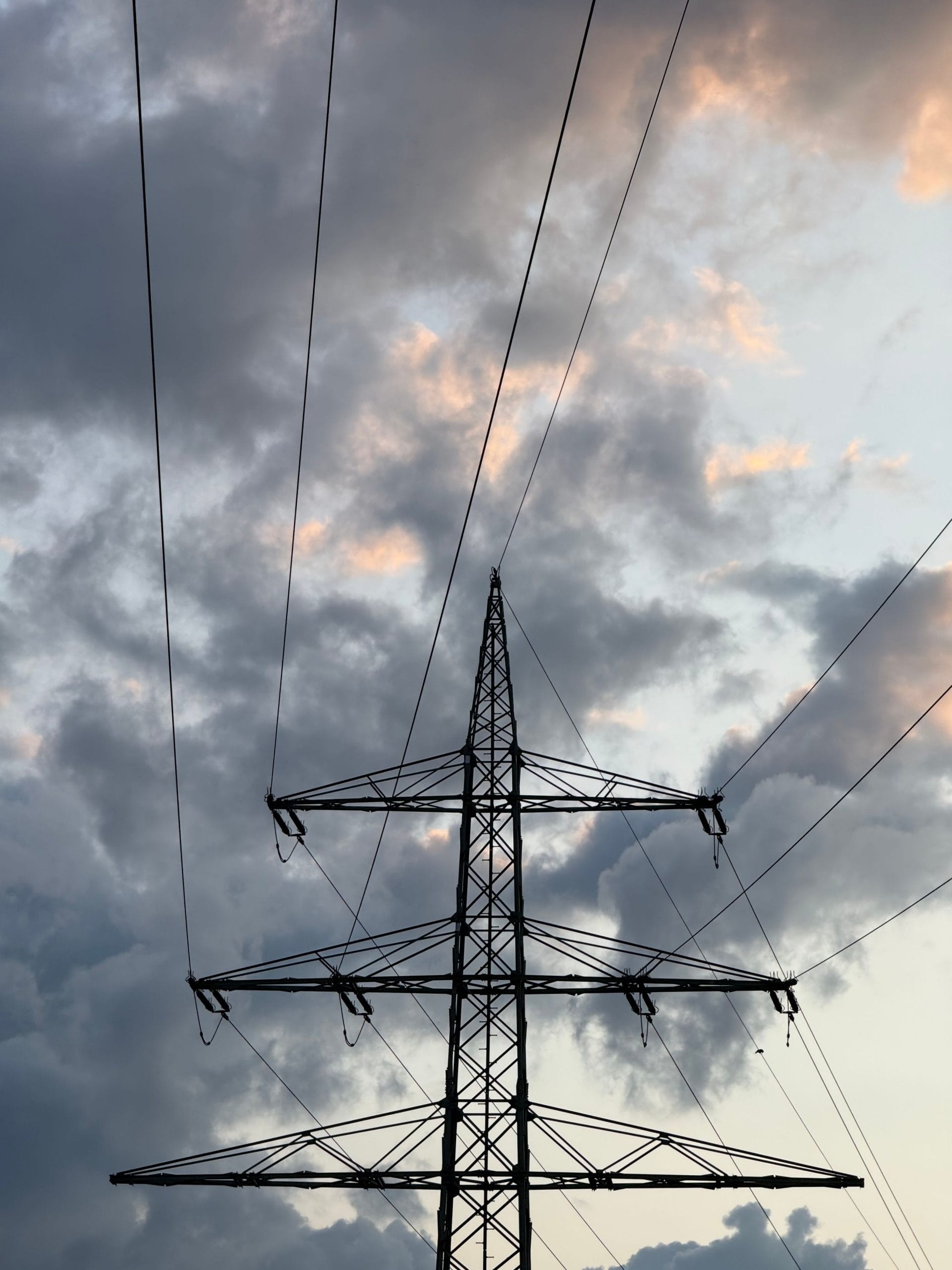 High tension power lines against a dramatic cloudy sky at dusk.